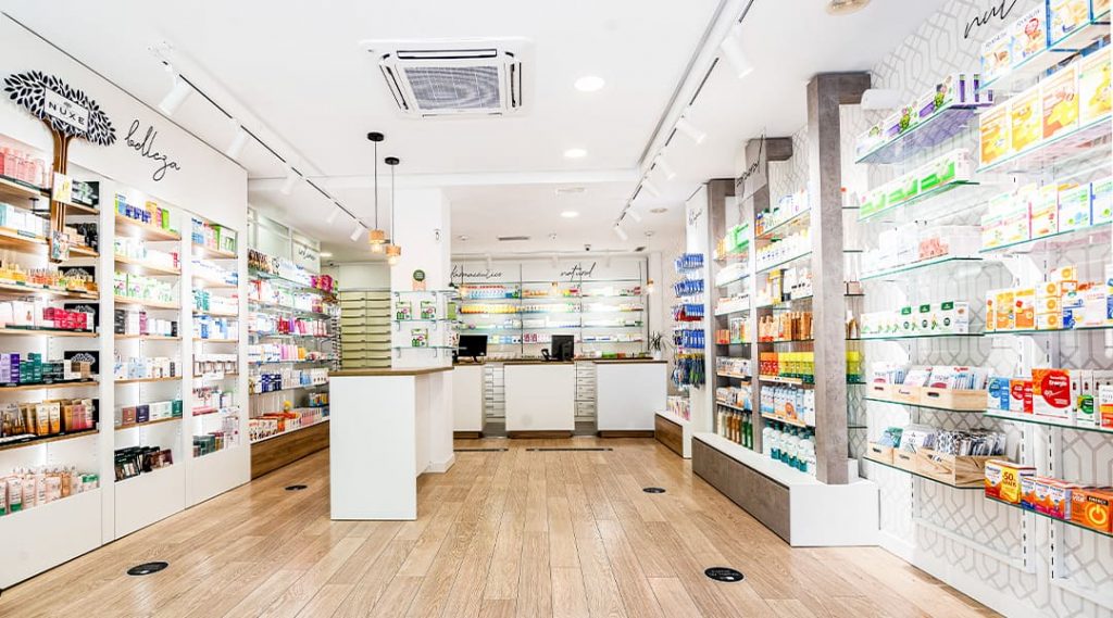Interior de farmacia moderna con estanterías iluminadas, productos organizados por categorías y mostrador central en un espacio amplio y luminoso.