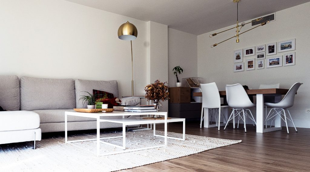 Salón moderno con sofá en tonos neutros, mesa de centro minimalista y zona de comedor integrada con mesa de madera, sillas blancas y lámparas decorativas.