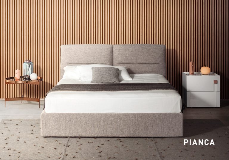 Dormitorio moderno con cama tapizada en tonos neutros, pared de listones de madera, mesillas laterales con lámparas decorativas y alfombra clara en el suelo